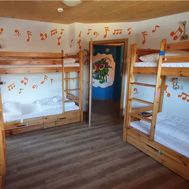 A cozy dormitory with wooden bunk beds. The walls are decorated with colorful musical notes.
