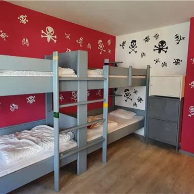 A children's room with bunk beds and red walls decorated with pirate symbols. There is also a mirror and a small refrigerator in the room.