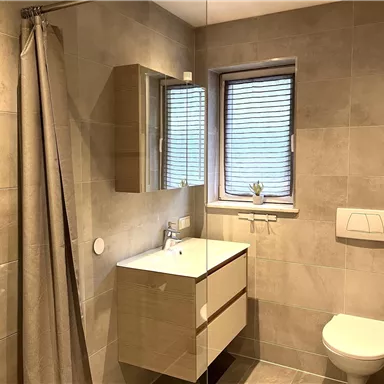 A modern bathroom with bright tiles and a shower. There is a sink with a mirror and a window with blinds.