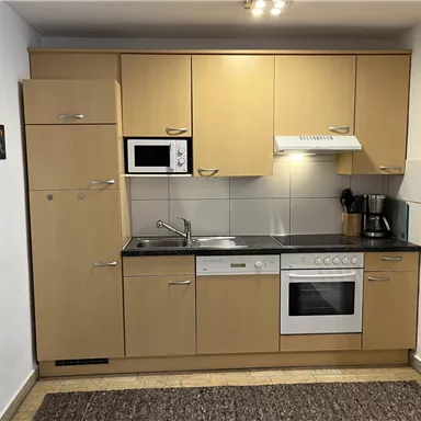 A modern kitchen with light wood cabinets and white appliances. It includes a stove, a sink, and a microwave.