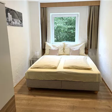 A cozy bedroom with a large bed and bright pillows.  
Windows with a view of greenery and modern furniture create an inviting atmosphere.