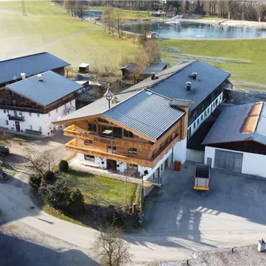 Ein traditionelles Gebäude umgeben von ländlicher Landschaft. Sanfte Hügel und eine ruhige Fläche im Hintergrund.