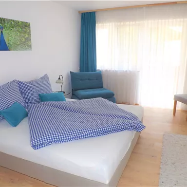 Ein gemütliches Schlafzimmer mit einem großen Bett und karierten Bettwäsche. Der Raum hat große Fenster und eine entspannende, helle Atmosphäre.