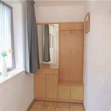 Ein heller Eingangsbereich mit einem Holzschrank und einer Garderobe. Das Fenster lässt viel Tageslicht herein.