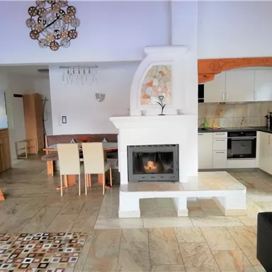 Ein moderner Wohnraum mit einer hellen Küche und einem gemütlichen Kamin. Der Raum hat eine freundliche Atmosphäre und warmen Holzdetails.