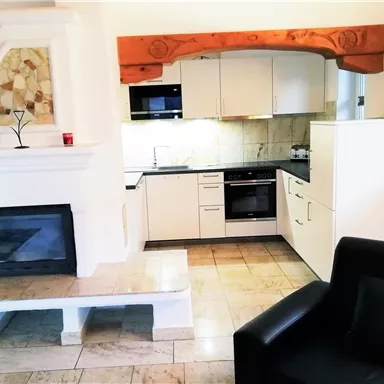 Eine moderne Küche mit einem eleganten Kamin und einem gemütlichen schwarzen Sessel. Die Ausstattung ist hell und einladend, ideal für entspanntes Kochen.