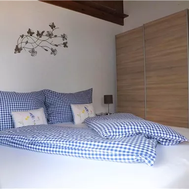 Ein gemütliches Schlafzimmer mit einem großen Bett und karierten Kissen. Im Hintergrund steht ein moderner Schrank aus Holz.