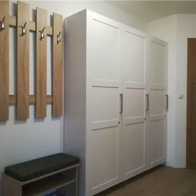 Ein moderner Flur mit einem weißen Schrank und einer Sitzbank. An der Wand hängen Holzkleiderhaken.