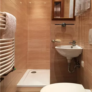 A small bathroom with a shower, a washbasin, and a toilet. The walls are in warm beige tones.