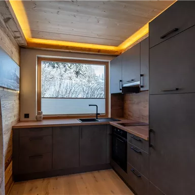A modern kitchen with wood paneling and a large window. The furnishings are functional and stylish with soft lighting.
