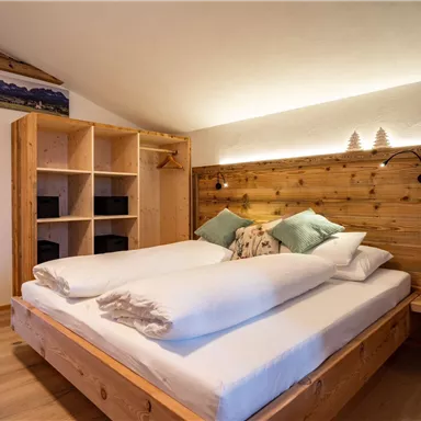 A cozy bedroom with a double bed and wooden shelves. The soft lighting creates a relaxing atmosphere.