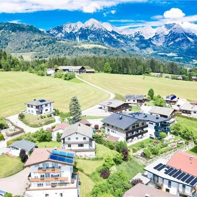 A picturesque landscape with houses in a green valley. Majestic mountains rise in the background under a clear blue sky.