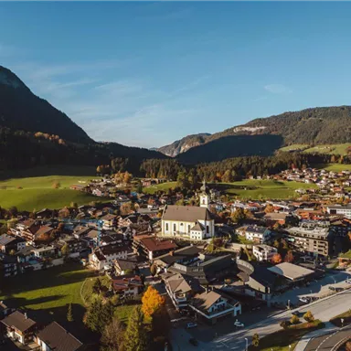 A picturesque view of a small village surrounded by mountains and green meadows. In the center stands a church, surrounded by traditional houses and colorful trees.