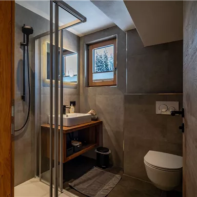 A modern bathroom with a shower and a wooden sink. Large tiles and a window create a bright atmosphere.