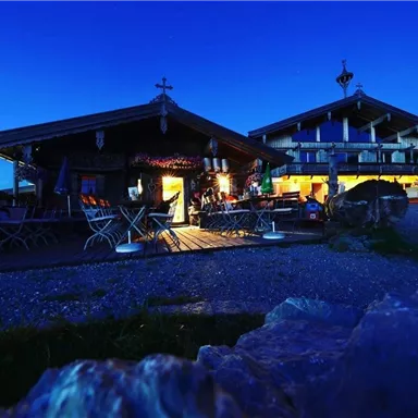 Eine Berghütte bei Nacht, beleuchtet von warmem Licht. Umgeben von einer ruhigen, ländlichen Landschaft.