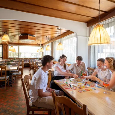 A group of five people is sitting at a table in a cozy restaurant. They are playing a game and enjoying drinks in a friendly atmosphere.