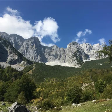An impressive mountain landscape with tall rocks and green forest floor. The sky is blue with scattered white clouds.