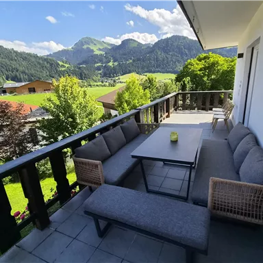 An inviting terrace with modern furniture and a beautiful view of the mountains. The surroundings are green and sunny, perfect for relaxing.
