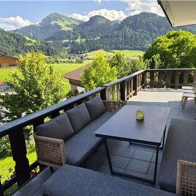 A cozy terrace with a modern seating area and a view of the mountains. The green landscape in the background creates a relaxed atmosphere.