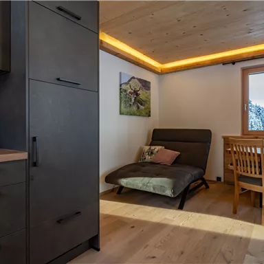 A modern room with wooden floors and a cozy seating area. A picture hangs on the wall and a window offers a view of the surroundings.