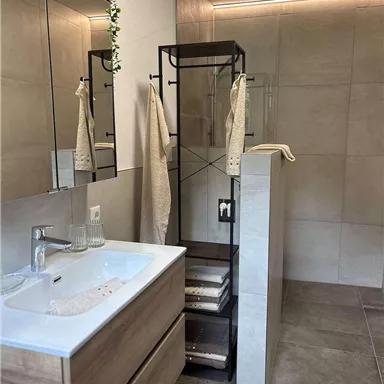Ein modernes Badezimmer mit einer stilvollen Dusche und einem Holzwaschbecken. Die Wände sind in neutralen Tönen gehalten, wodurch der Raum hell und einladend wirkt.