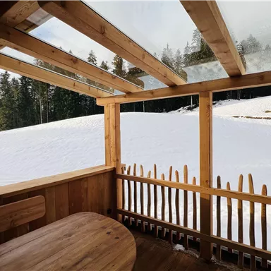A cozy wooden room with a table and a view of a snow-covered landscape. In the background, trees and a quiet, snowy plain can be seen.