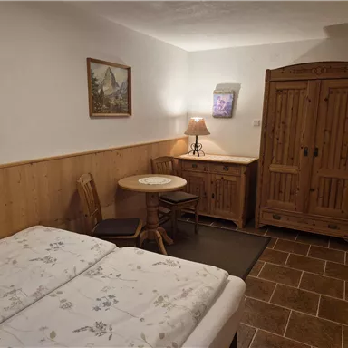 A cozy bedroom with two beds and a table. The room features wooden furniture and a window with soft light.