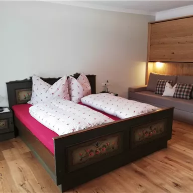 Ein gemütliches Schlafzimmer mit einem großen Doppelbett und einer modernen Sitzecke. Der Raum hat schöne Holzdetails und eine einladende Atmosphäre.