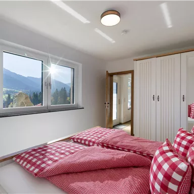 A cozy bedroom with a large window that offers a view of the mountains. The bed is decorated with red and white checkered pillows and blankets.