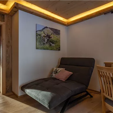 A cozy room with a comfortable chair and a wooden table. A picture of a landscape hangs on the wall.