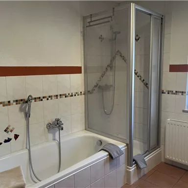 A modern bathroom with a bathtub and a separate shower. The walls are tiled and there is a window for daylight.
