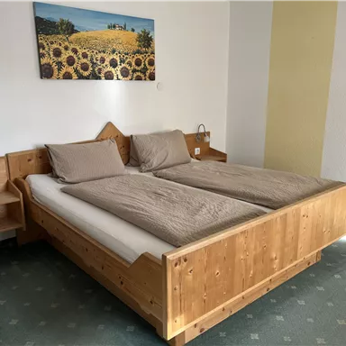 A cozy bedroom with a large wooden bed and two pillows. On the wall hangs a picture of sunflowers, and there are nightstands with lamps.