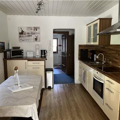 A modern kitchen with wooden cladding and bright elements. The table is set with a white cloth and there are various kitchen appliances.