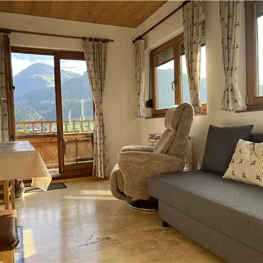 A cozy living room with a view of the mountains. There is a gray sofa, a television, and a comfortable armchair.