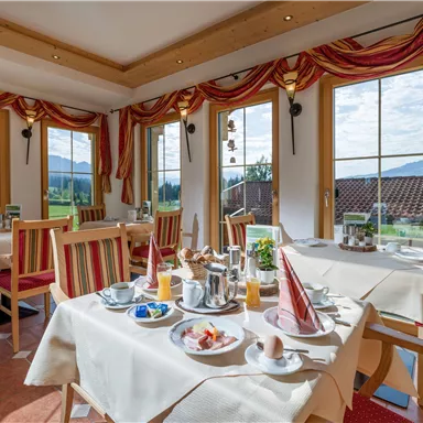 An inviting breakfast room with bright windows and a beautiful view. Various breakfast dishes and drinks are arranged on the tables.