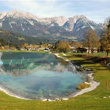Eine malerische Aussicht auf einen klaren See, umgeben von grünen Wiesen und majestätischen Bergen. Die ruhige Wasseroberfläche spiegelt die umliegende Natur wider.