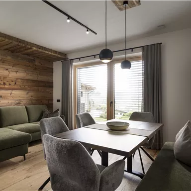 A stylish living room with a green couch and a modern dining table.
Large windows let in plenty of light and provide a view outside.