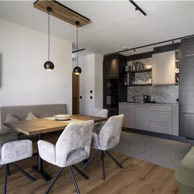 A modern dining room with a wooden table and comfortable chairs. In the background, a stylish kitchen is visible.