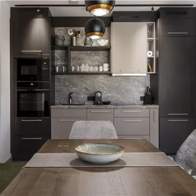 A modern kitchen with dark cabinets and white accents. A dining area with a wooden tray and comfortable chairs is also visible.