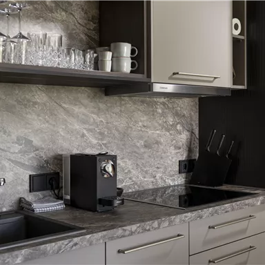 A modern kitchen with an elegant countertop and minimalist furniture. There are glasses, mugs, and a coffee machine on the countertop.