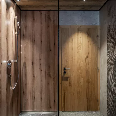 A modern shower with wood paneling and a glass partition. In the background, a door with a simple design is visible.