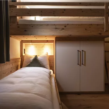 A cozy bedroom with a loft bed and a single bed side. The room is made of wood and features a modern wardrobe.