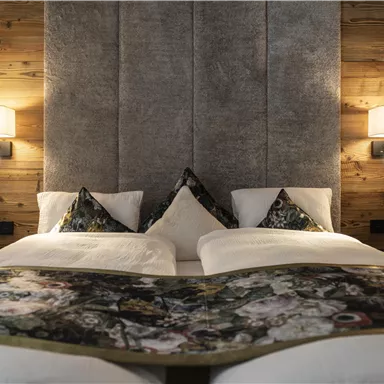 A stylish bedroom with two beds and a cozy wooden paneling. An elegant headboard and decorative pillows complete the ambiance.