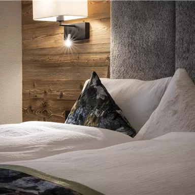 A cozy bedroom with a modern bed and decorative cushions. Soft light creates an inviting atmosphere.