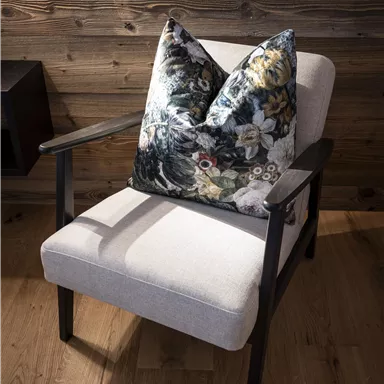 A comfortable armchair with a colorful cushion stands in front of a wooden wall. The room has a warm and inviting atmosphere.