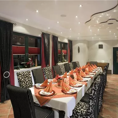 An elegant dining room with a long table set with served plates and decorated napkins. The walls are adorned with stylish curtains and the lighting creates a cozy atmosphere.