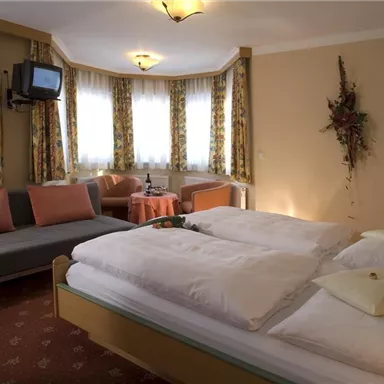 A cozy bedroom with two beds, a sofa, and windows that let in plenty of light. The stylish decor creates an inviting atmosphere.
