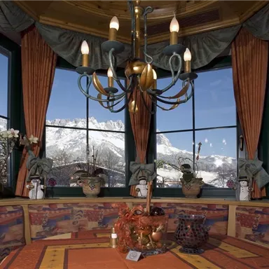 A cozy room with windows that offer a view of snow-covered mountains. The decor is rustic with plants and a chandelier.