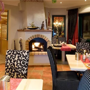 A cozy restaurant with an open fireplace. The tables are festively laid, and the decor is modern with elegant chairs.