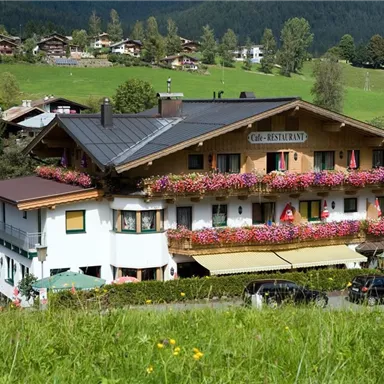 A picturesque inn with blooming balcony plants in the Alps. The surrounding landscape is green and hilly, perfect for a relaxing getaway.